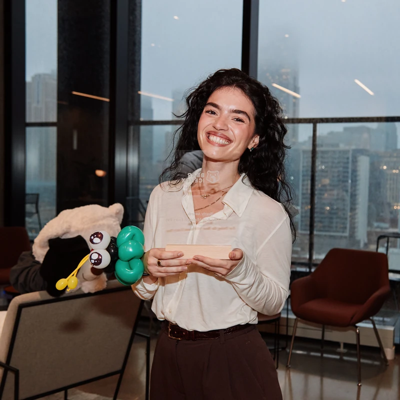 A corporate employee smiling with an award and a ladybug balloon bracelet