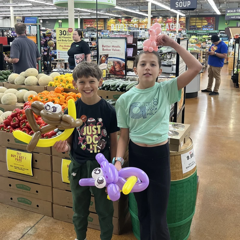 Two children posing with their balloon animals at a Fresh Thyme Market customer appreciation day in Chicago