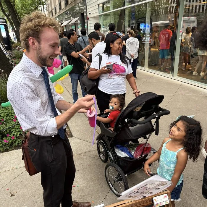 Michael Romani twisting a balloon for a young girl, Labor Day weekend 2026