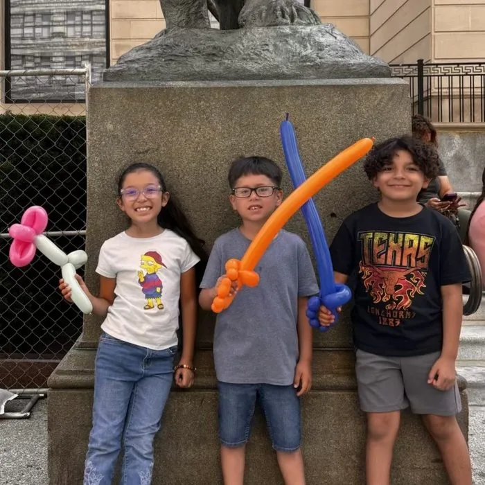 Three kids with their balloon swords and a balloon flower outside the Art Institute of Chicago, late July 2026