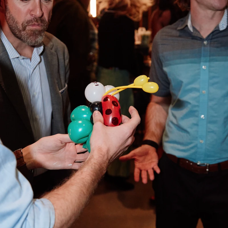 Michael Romani handing a ladybug balloon bracelet to a guest at a corporate event
