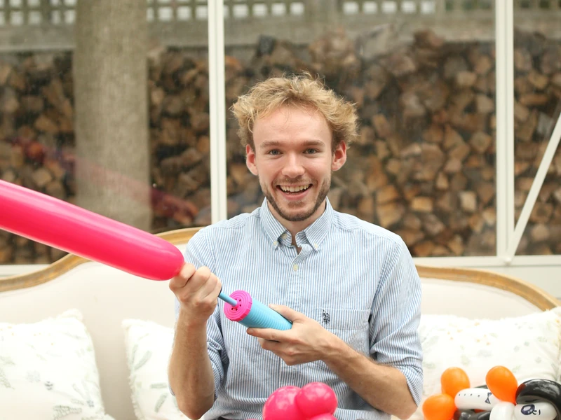 Michael Romani smiling while blowing up a pink balloon