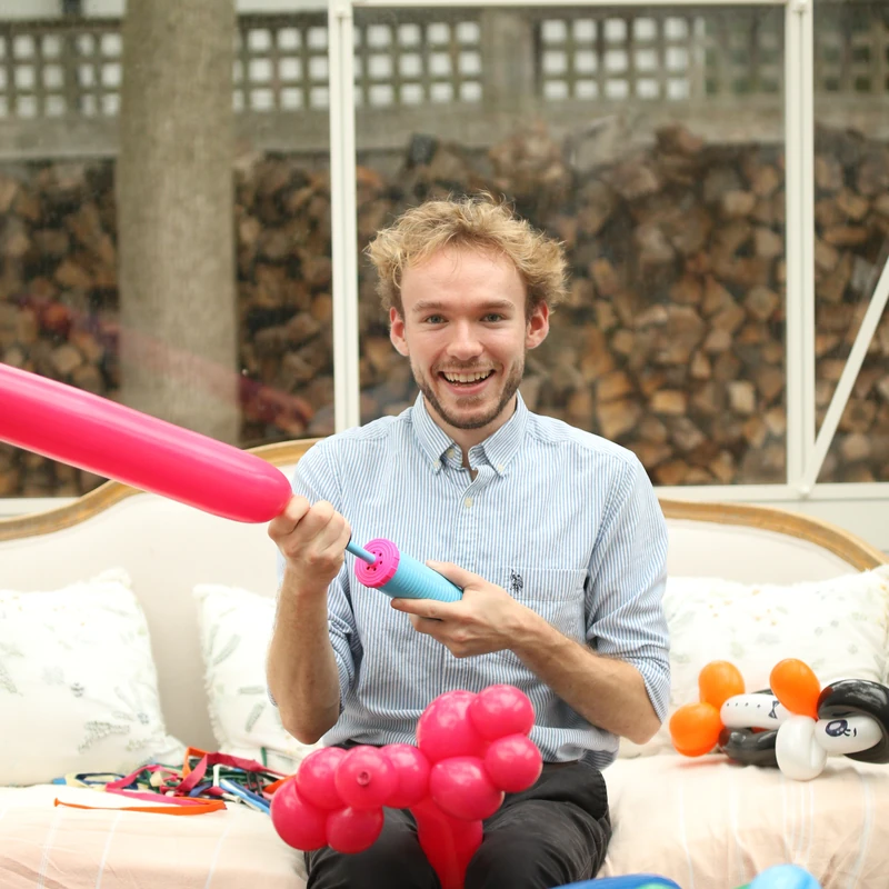Michael Romani smiling while blowing up a pink balloon