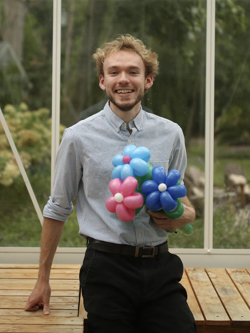 Michael Romani, Chicago balloon artist, leaning on a table and smiling with balloon flowers